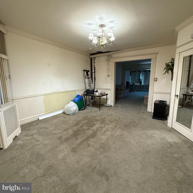 carpeted empty room with ornamental molding and a chandelier