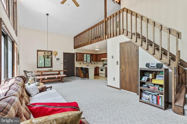 living room with light carpet, a high ceiling, and ceiling fan with notable chandelier