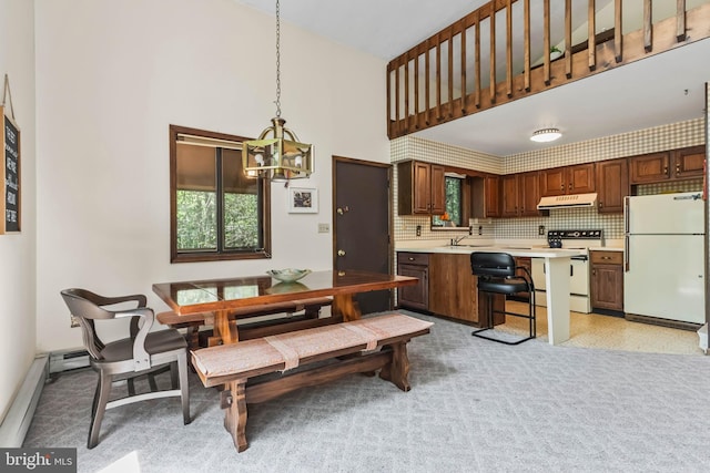 kitchen with a towering ceiling, tasteful backsplash, white appliances, pendant lighting, and a breakfast bar area