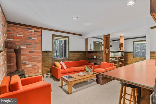 living room featuring baseboard heating, a wood stove, wooden walls, and ornamental molding