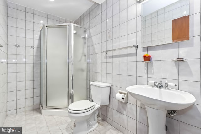 bathroom with tile patterned floors, a shower with shower door, tile walls, and toilet