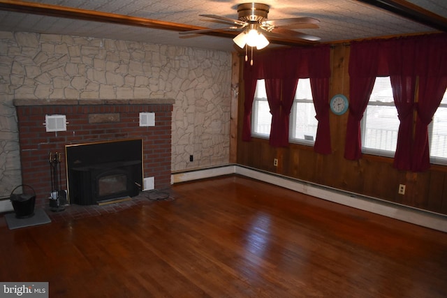 unfurnished living room featuring wood walls, baseboard heating, wood finished floors, and a ceiling fan