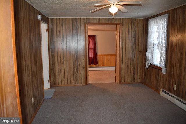 unfurnished room with a baseboard heating unit, carpet, wood walls, and ceiling fan