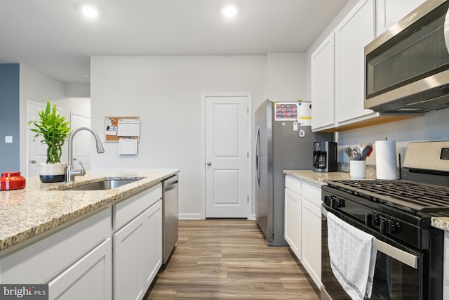 kitchen with light stone countertops, sink, appliances with stainless steel finishes, white cabinets, and hardwood / wood-style flooring