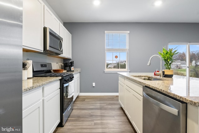 kitchen with wood-type flooring, sink, appliances with stainless steel finishes, light stone counters, and white cabinetry