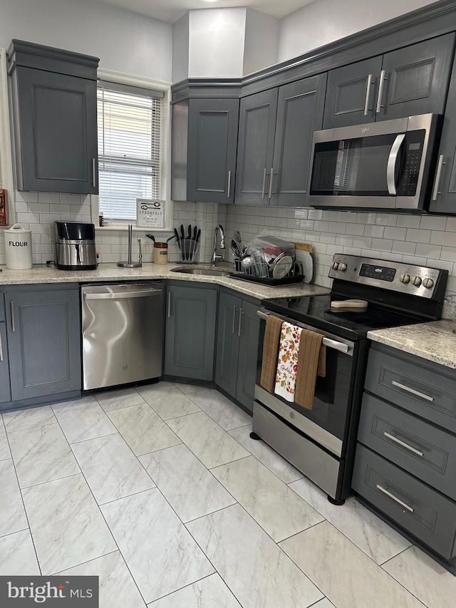 kitchen with decorative backsplash, light stone counters, sink, and appliances with stainless steel finishes