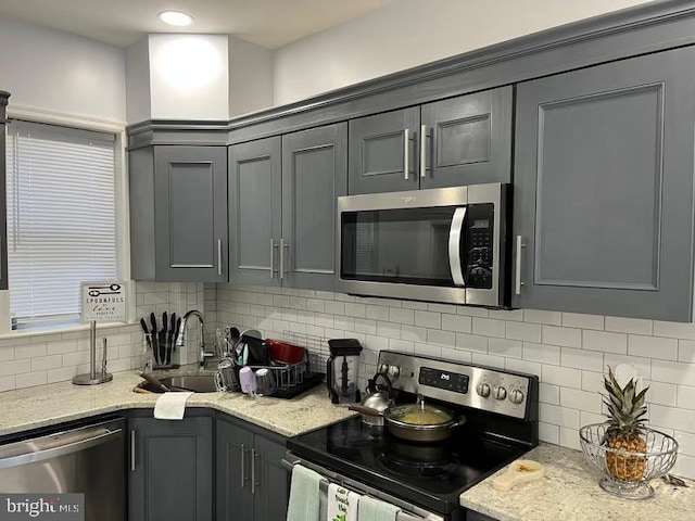 kitchen featuring light stone countertops, backsplash, stainless steel appliances, sink, and gray cabinets