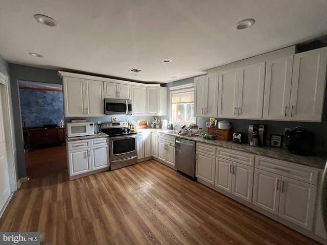 kitchen with stainless steel appliances, white cabinetry, hardwood / wood-style flooring, and sink