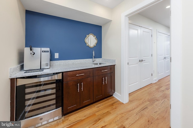 bar with light stone countertops, sink, wine cooler, light hardwood / wood-style floors, and dark brown cabinets