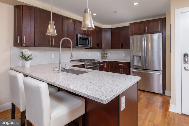 kitchen featuring hanging light fixtures, light hardwood / wood-style flooring, kitchen peninsula, a kitchen bar, and appliances with stainless steel finishes