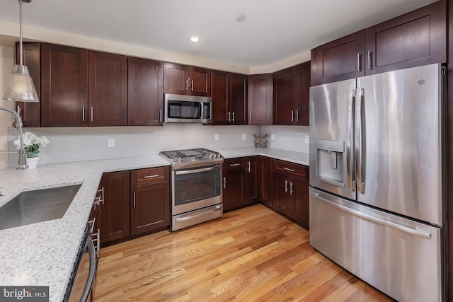 kitchen featuring sink, stainless steel appliances, light stone counters, light hardwood / wood-style floors, and decorative light fixtures