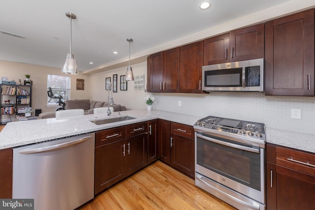 kitchen with kitchen peninsula, light wood-type flooring, light stone counters, stainless steel appliances, and hanging light fixtures