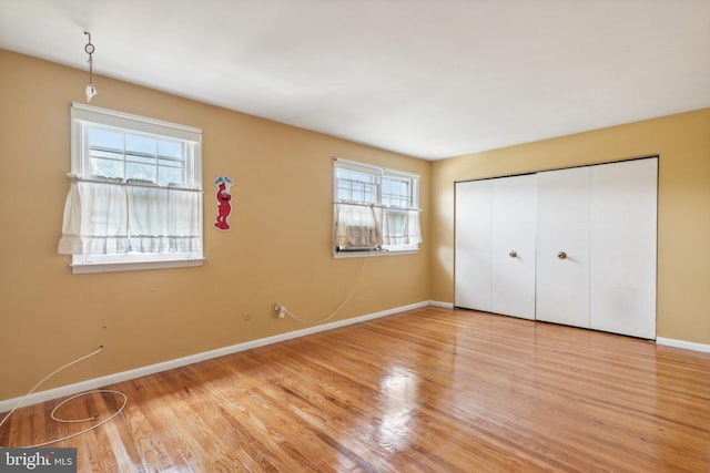 unfurnished bedroom with a closet, light wood-type flooring, and multiple windows