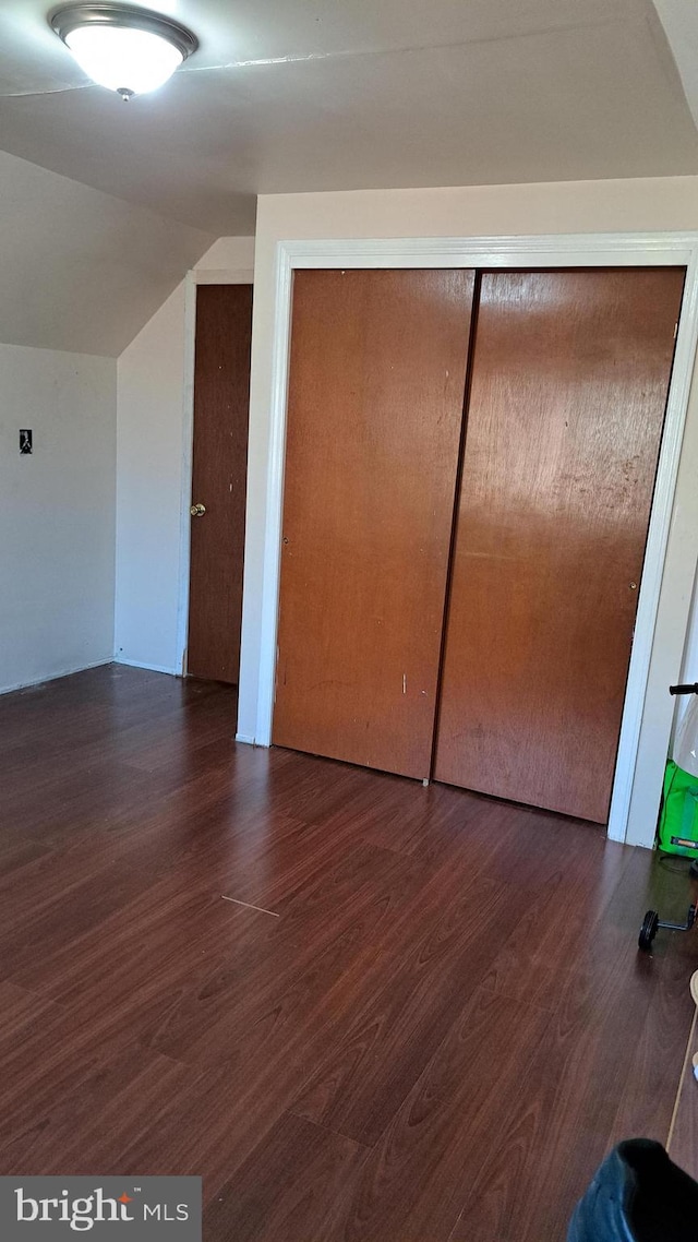 unfurnished bedroom featuring lofted ceiling, a closet, and dark wood-type flooring