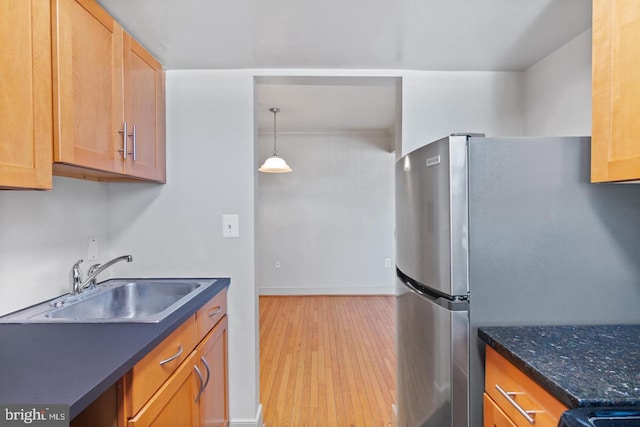 kitchen featuring sink, hanging light fixtures, stainless steel fridge, dark stone counters, and light hardwood / wood-style floors