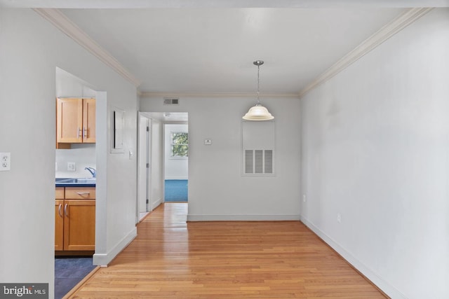 unfurnished dining area featuring crown molding, sink, and light wood-type flooring