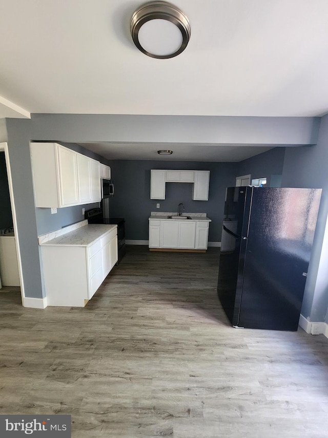 kitchen featuring black fridge, white cabinets, and hardwood / wood-style flooring