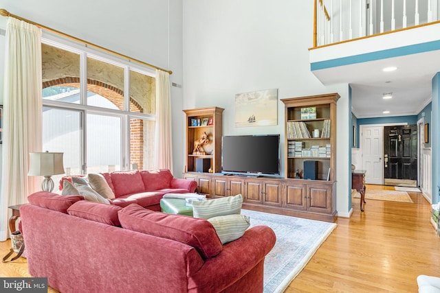 living room with light hardwood / wood-style flooring, a high ceiling, and ornamental molding