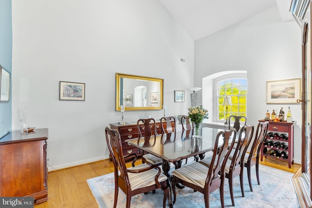 dining room with high vaulted ceiling and light hardwood / wood-style flooring