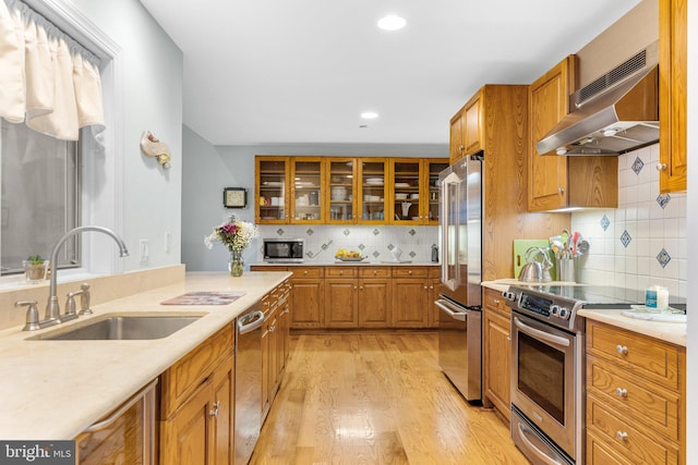 kitchen featuring decorative backsplash, light wood-type flooring, stainless steel appliances, sink, and exhaust hood