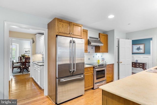 kitchen with backsplash, stainless steel appliances, extractor fan, and light hardwood / wood-style floors