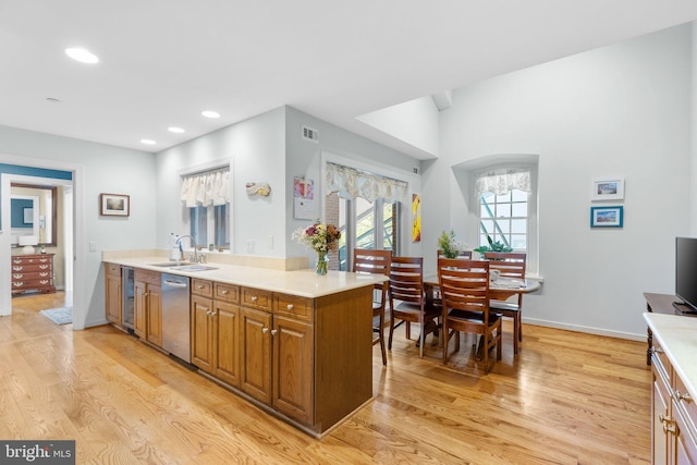 kitchen featuring stainless steel dishwasher, kitchen peninsula, sink, and light hardwood / wood-style flooring