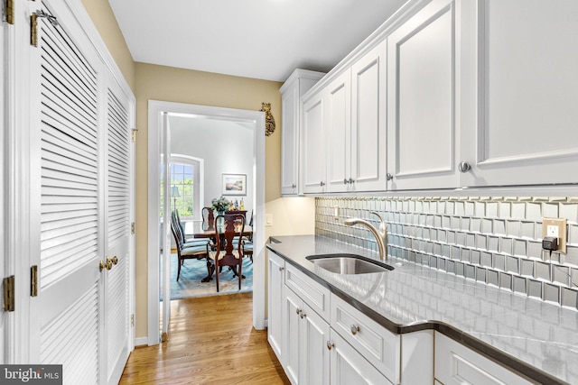 kitchen featuring sink, light stone counters, light hardwood / wood-style flooring, backsplash, and white cabinets