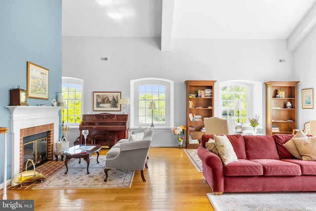 living room featuring beamed ceiling, light wood-type flooring, a fireplace, and a towering ceiling