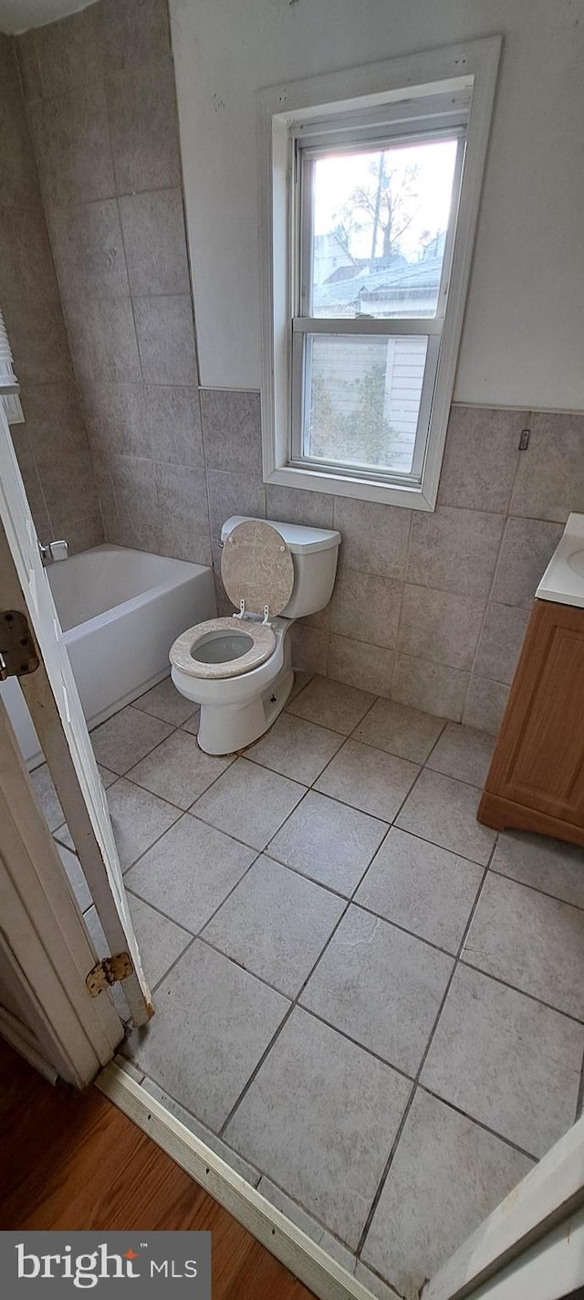 bathroom with a tub to relax in, tile patterned floors, vanity, tile walls, and toilet