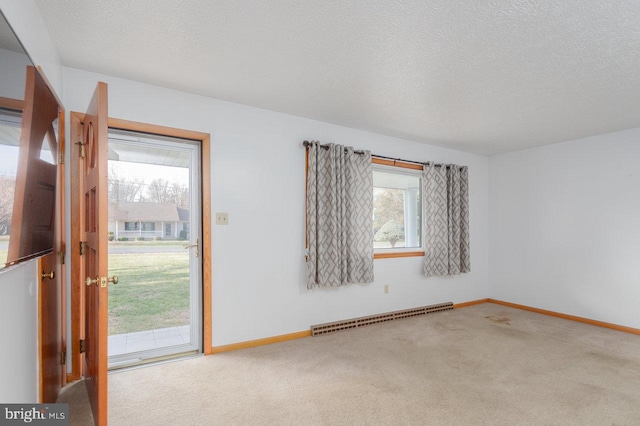 carpeted empty room with a healthy amount of sunlight, a textured ceiling, and a baseboard heating unit