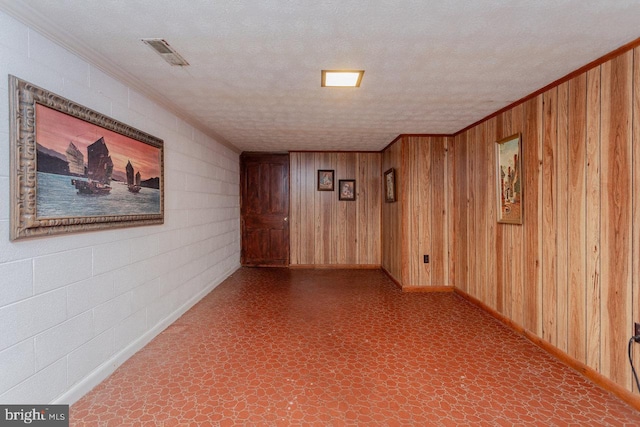 spare room with wood walls, a textured ceiling, and ornamental molding