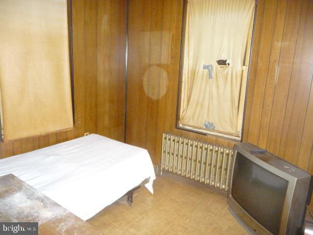 bedroom featuring radiator heating unit, light parquet flooring, a closet, and wooden walls