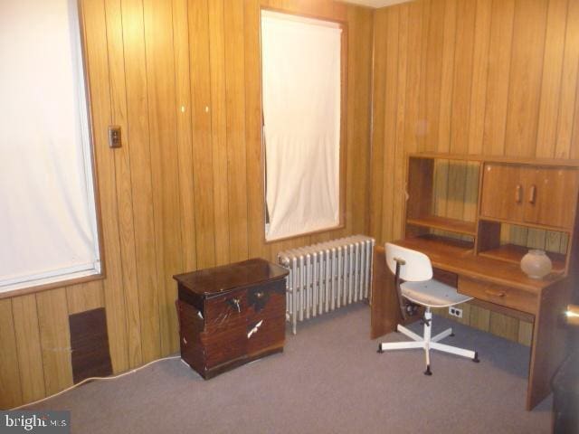 office featuring carpet flooring, radiator heating unit, and wood walls