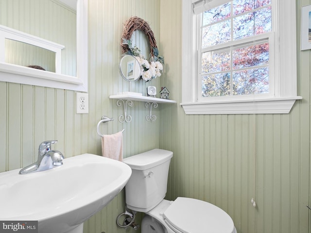 bathroom featuring toilet, sink, and wooden walls