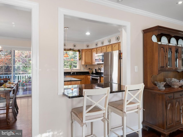 kitchen featuring stainless steel appliances, dark hardwood / wood-style floors, kitchen peninsula, crown molding, and a breakfast bar area