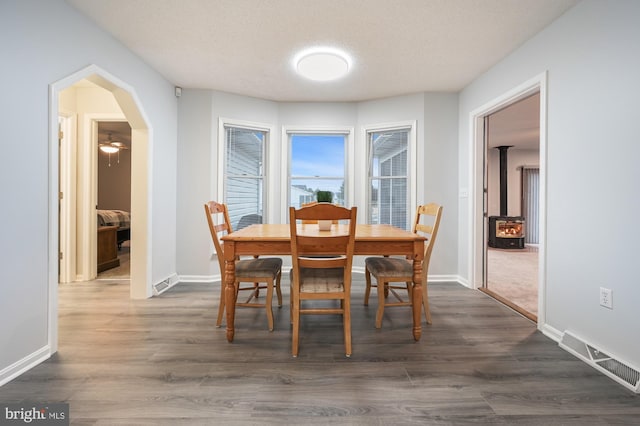 dining space with a textured ceiling, a wood stove, and dark wood-type flooring