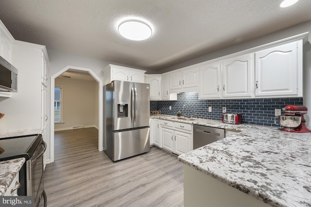 kitchen featuring white cabinetry, sink, light stone countertops, tasteful backsplash, and appliances with stainless steel finishes