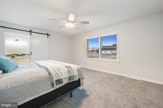 carpeted bedroom featuring a barn door and ceiling fan