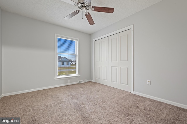 unfurnished bedroom with carpet, ceiling fan, a textured ceiling, and a closet