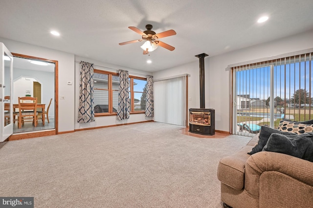 carpeted living room with a wood stove and ceiling fan