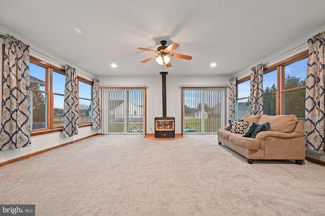 unfurnished living room with carpet flooring, a wood stove, and ceiling fan