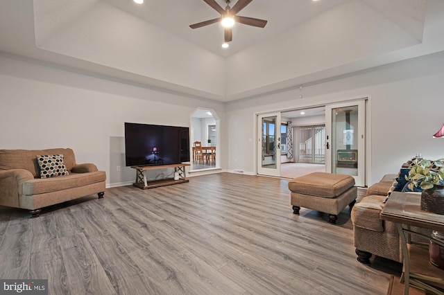 living room with a high ceiling, light wood-type flooring, a tray ceiling, and ceiling fan