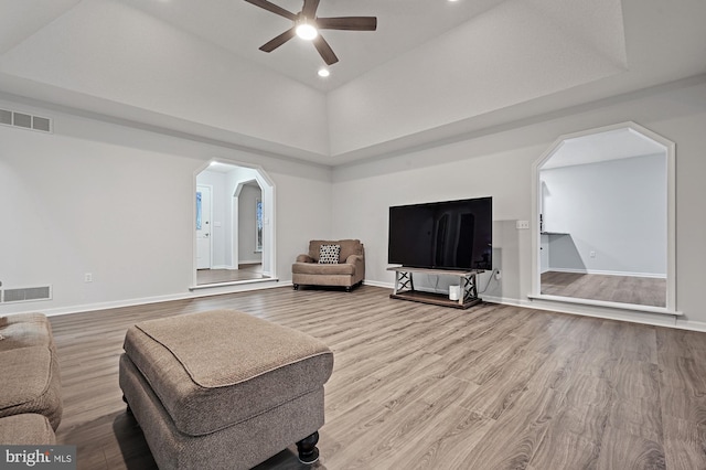 living room featuring a towering ceiling, hardwood / wood-style flooring, a raised ceiling, and ceiling fan