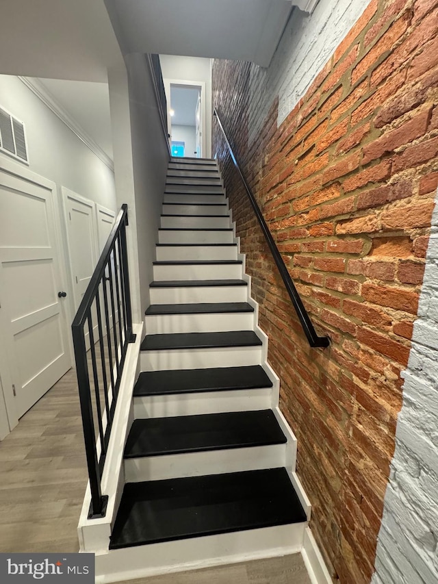 stairway with ornamental molding, brick wall, and hardwood / wood-style flooring