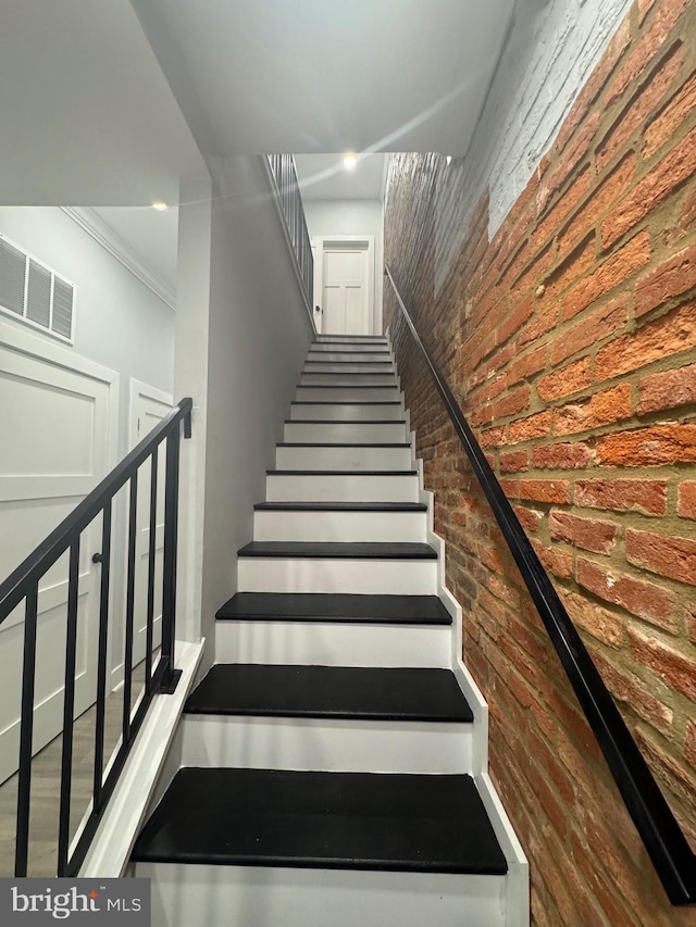 stairway featuring crown molding, brick wall, and hardwood / wood-style flooring