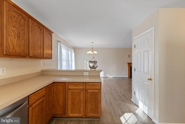 kitchen with an inviting chandelier, hanging light fixtures, stainless steel dishwasher, light hardwood / wood-style floors, and kitchen peninsula