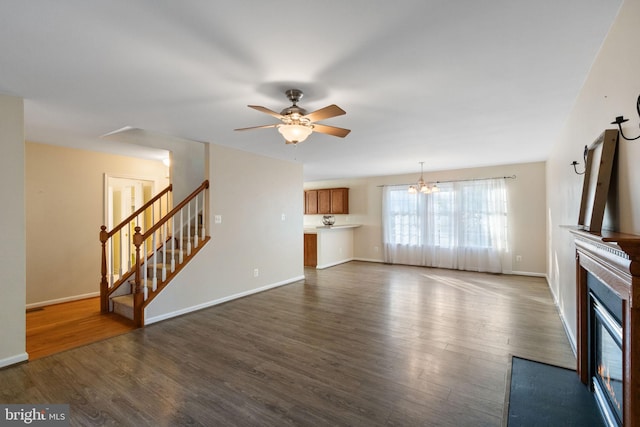 unfurnished living room with ceiling fan with notable chandelier and dark wood-type flooring