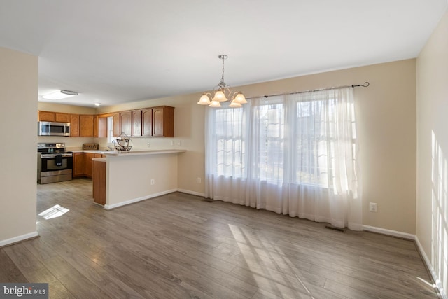 kitchen featuring an inviting chandelier, kitchen peninsula, appliances with stainless steel finishes, and light hardwood / wood-style flooring