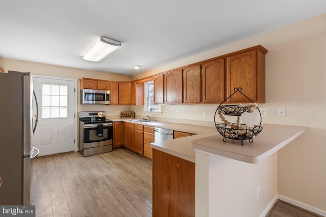 kitchen with sink, light wood-type flooring, kitchen peninsula, and appliances with stainless steel finishes