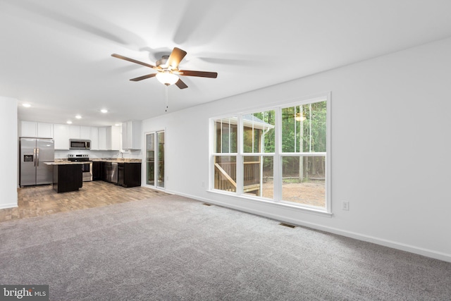 unfurnished living room featuring ceiling fan, light colored carpet, and sink